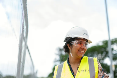 A smiling female international engineering student wears a hard hat on the job site