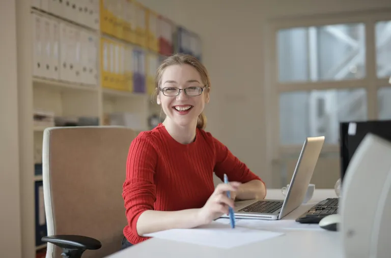 A student at a desk smiles while deciding when to apply to grad school