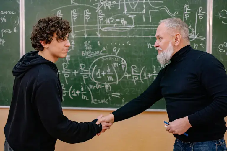 A student earning his second bachelor's degree shakes hands with a professor.