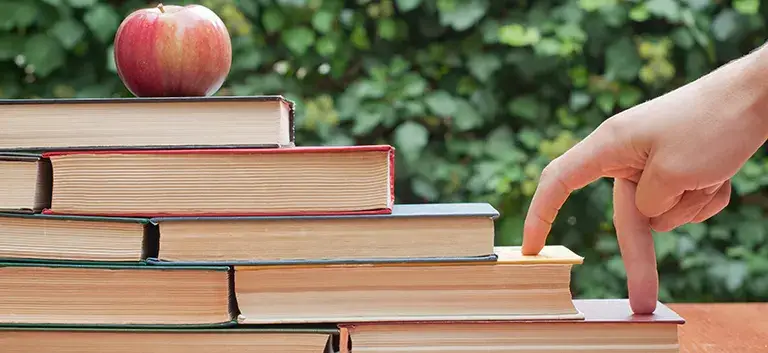 a hand climbing books to get the apple